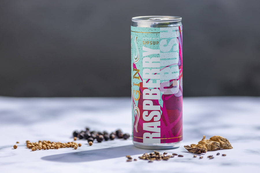 A can called Raspberry Crush cocktail on table with juniper and other botanicals at the base